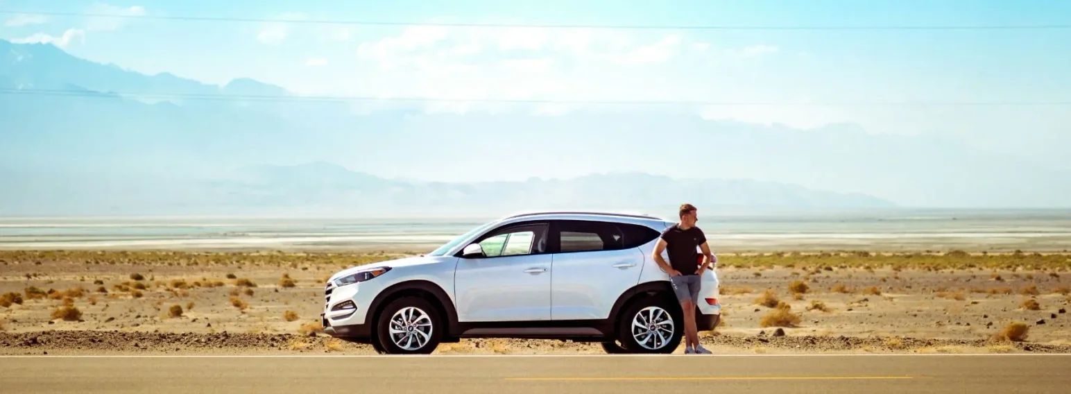 Car parked in the desert with a man leaning against it, representing the freedom of owning a vehicle through AAA Finance car loans.