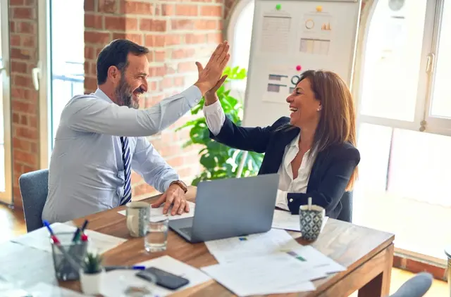 Two happy business professionals high-fiving, celebrating a car loan with no proof of income approval.