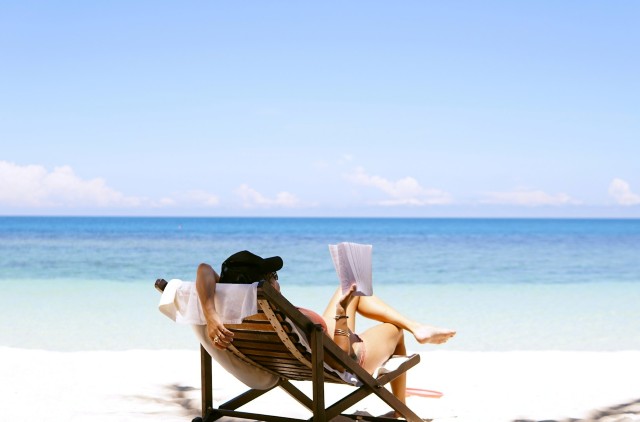 Woman sitting on a beach reading a book in a beach chair, enjoying a holiday showing one way to use a personal loan.