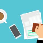 Illustration of an approved car loan application form with a bold “approved” stamp, coffee cup, and mobile phone on the desk – representing how easy it is to apply for a car loan.